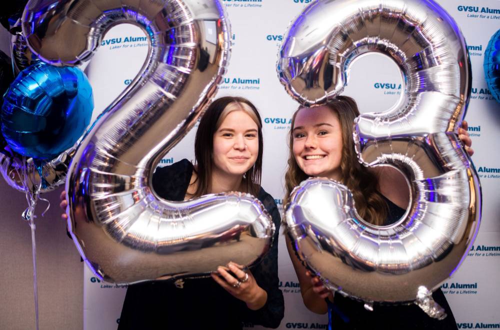 Two grads peek through the 2023 balloons for a photo